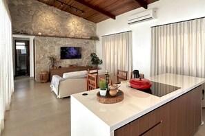 Una cocina moderna con una pared de acento de piedra, un televisor de pantalla plana y una zona de comedor con un sofá y una mesa de centro.