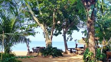 A beach path leading to a wooden deck with chairs and a table, surrounded by trees and vegetation.