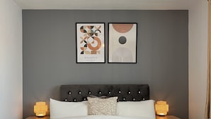 Un dormitorio moderno con un cabecero capitonado, una cama grande con ropa de cama blanca, dos lámparas de noche y arte abstracto en la pared.