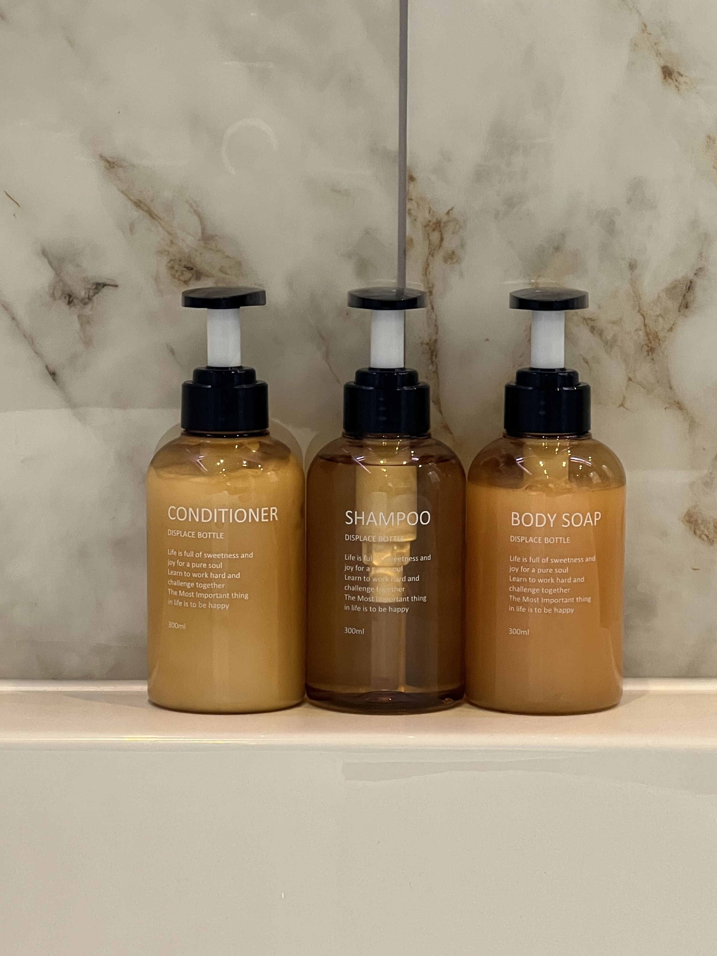 Three bottles of toiletries on a marble countertop.