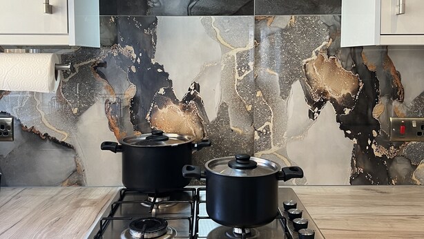 Una cocina moderna con dos ollas negras sobre una estufa a gas, una campana extractora de acero inoxidable y un salpicadero de mármol con diseño envejecido.