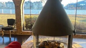 A stone fireplace with a chimney, a red sofa, and a view of a body of water through arched windows.