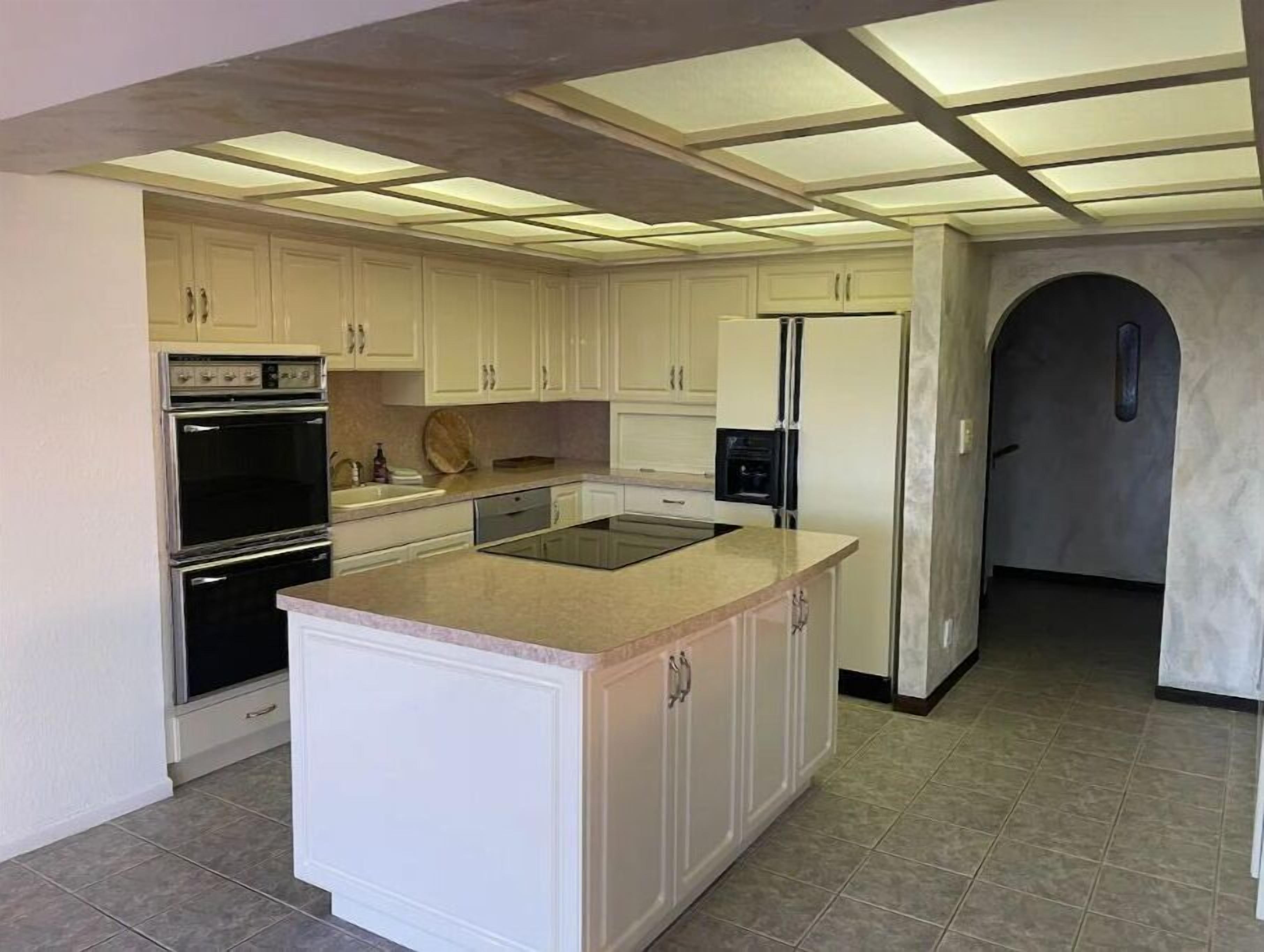 Une cuisine moderne avec des meubles blancs, un îlot central, un four encastré et un réfrigérateur.