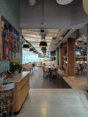 A modern restaurant with a wooden counter, dining tables, and hanging pendant lights.