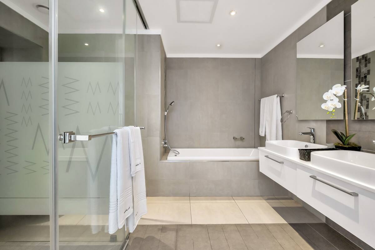 A modern bathroom with a glass shower enclosure, a bathtub, and a vanity with a sink and mirror.