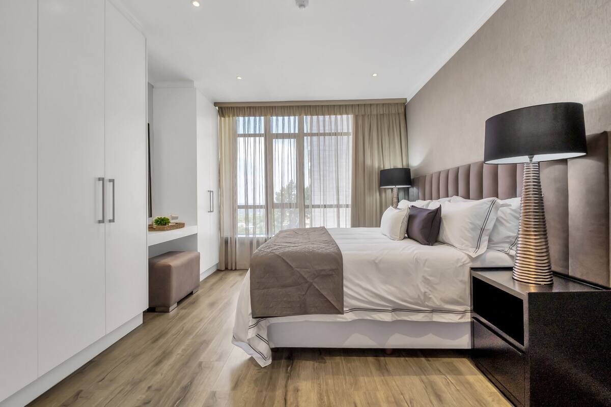 A modern bedroom with a bed, bedside table, lamp, and wardrobe.