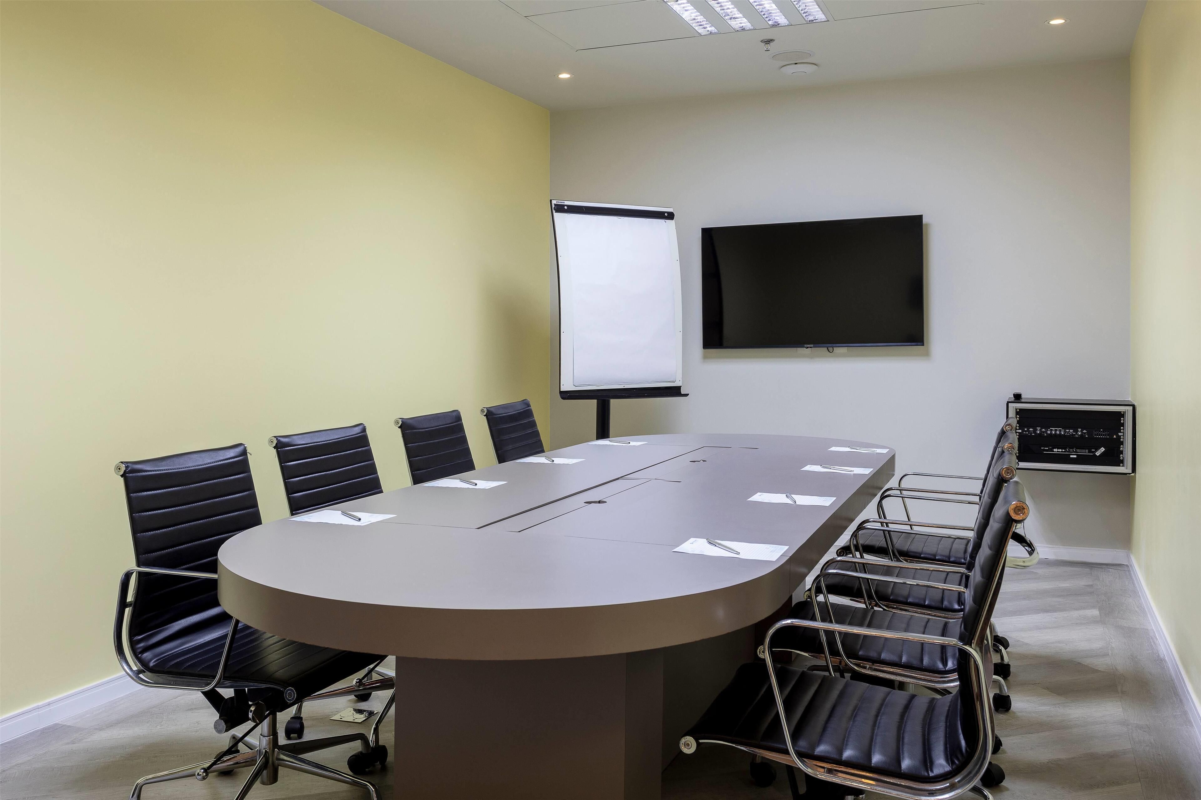 A conference room with a large table, six chairs, a projector screen, and a TV on the wall.