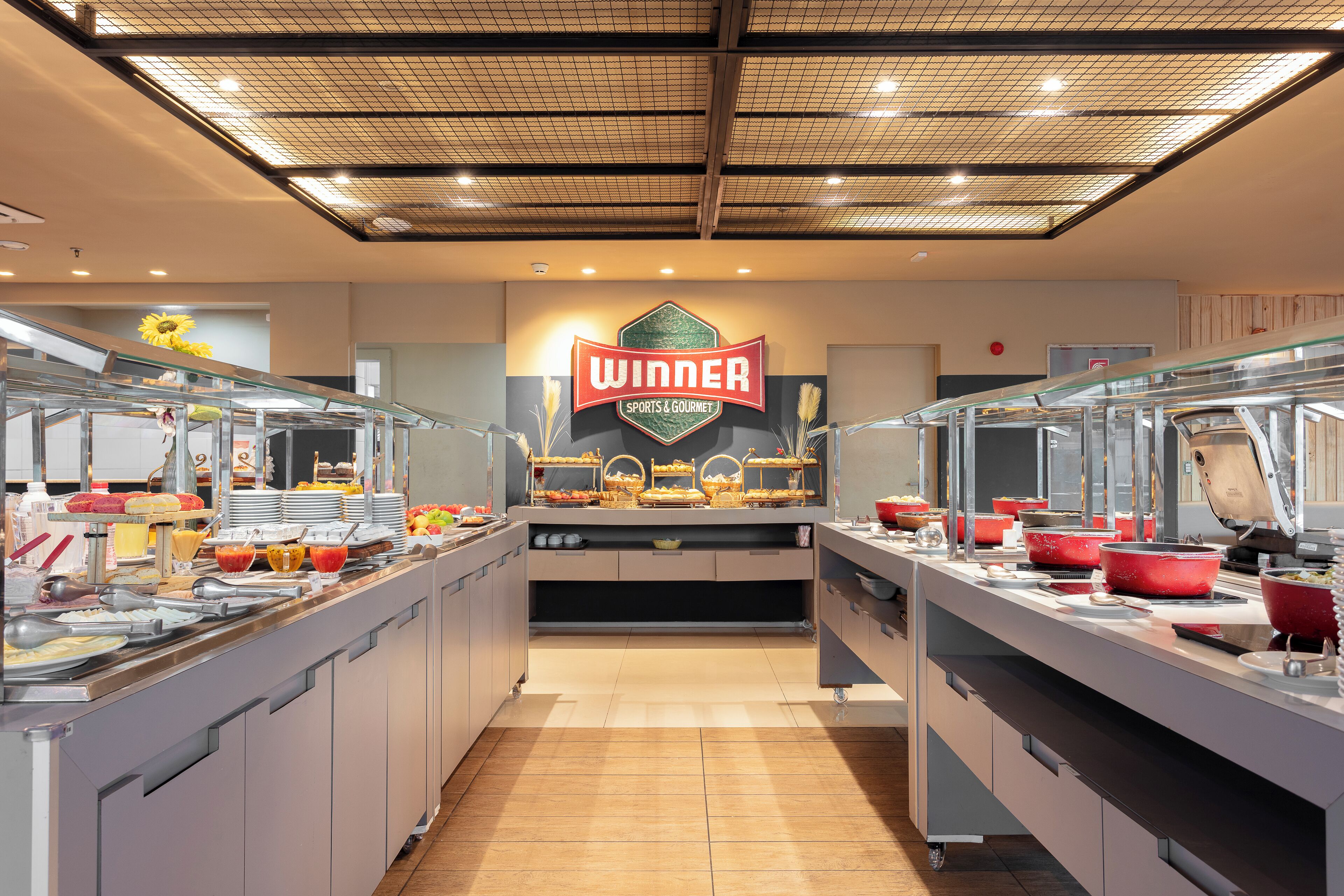 A buffet area with a 'WINNER SPORTS & GOURMET' sign, multiple food stations, and a clean, modern design.