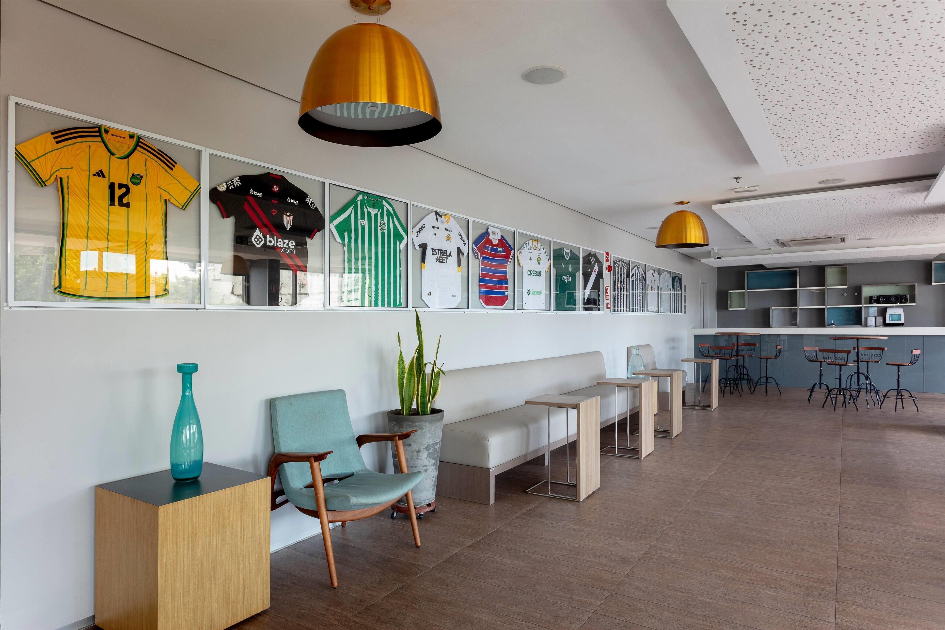 Un intérieur moderne agrémenté d’un mur où sont accrochés des maillots de sport encadrés, d’un espace détente avec un banc et des chaises, et d’un bar avec des tabourets.