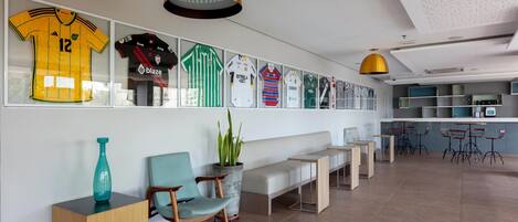 A modern interior with a wall of framed sports jerseys, a seating area with a bench and chairs, and a bar area with stools.