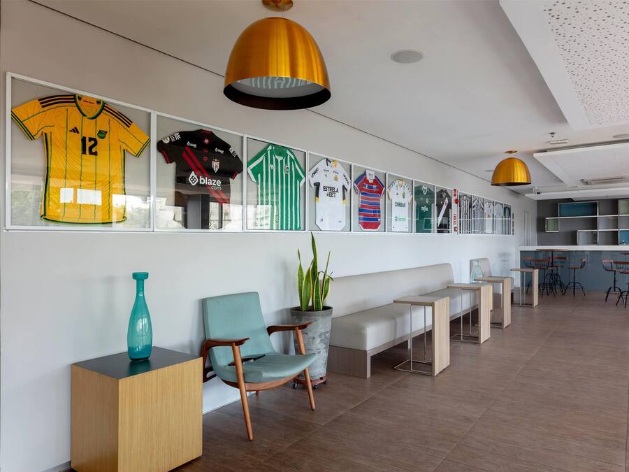 A modern interior with a wall of framed sports jerseys, a seating area with a bench and chairs, and a bar area with stools.