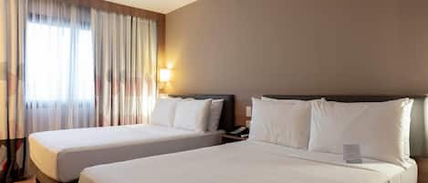 Una habitación de hotel con dos camas, una mesita de noche, una lámpara y una ventana con cortinas.