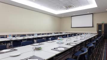 A conference room with long tables, chairs, water bottles, and a projector screen.