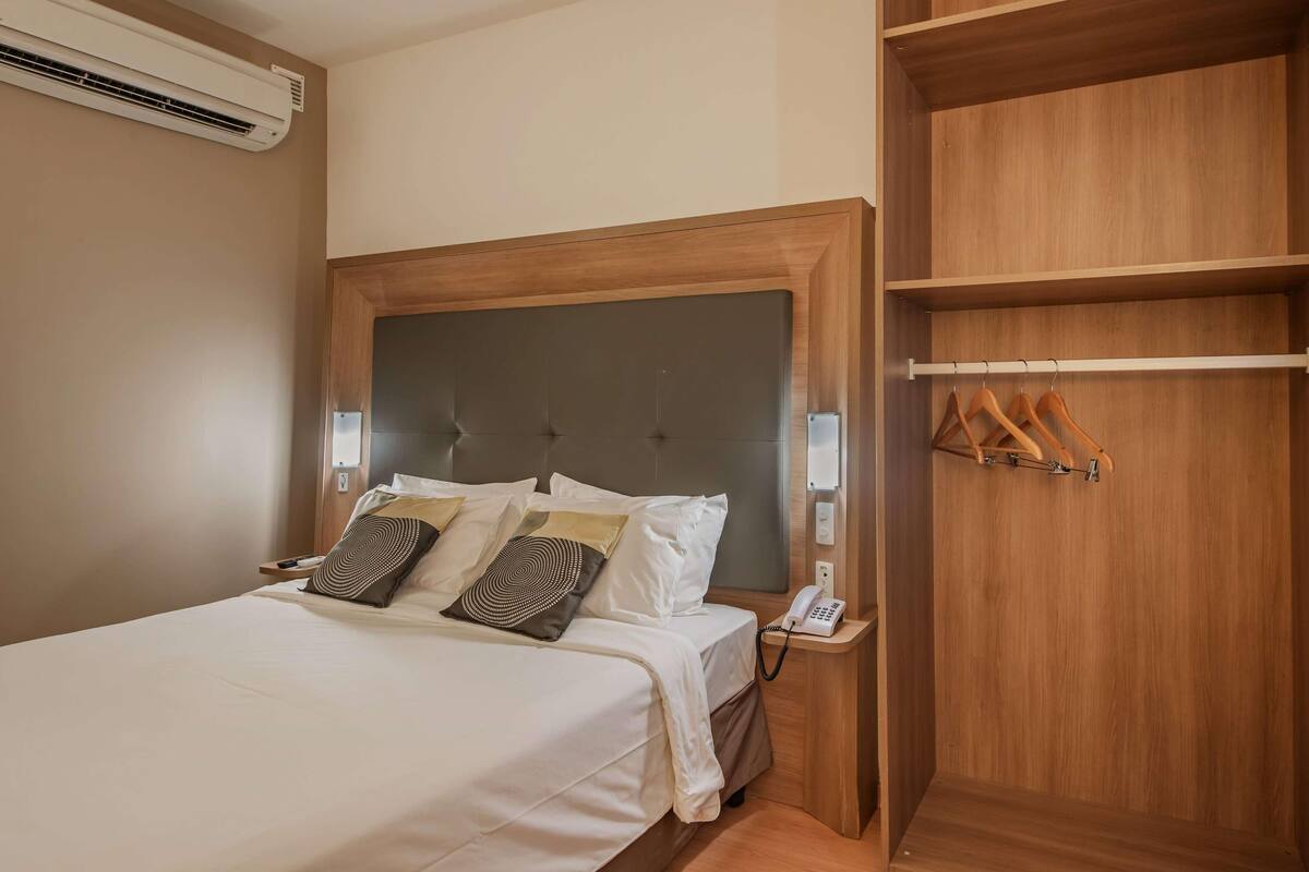 Une chambre d’hôtel avec un lit, un téléphone sur la table de chevet et une armoire en bois.