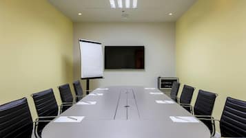 Une salle de conférence avec une longue table, des chaises noires, un tableau blanc et un écran de projection.