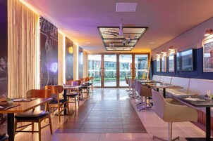 Un restaurante moderno con mesas y sillas de madera, un amplio ventanal que da al exterior y cuadros enmarcados en las paredes.
