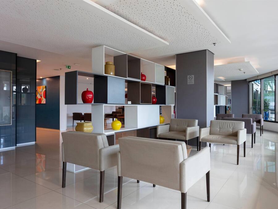 A modern lobby with a seating area, a white reception desk, and a large window providing a view of the outdoors.
