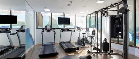 Un gimnasio con cintas de correr, bicicletas estáticas y una máquina de pesas.
