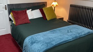 Una cama con una colcha verde oscuro, una manta azul y varias almohadas de diferentes colores.