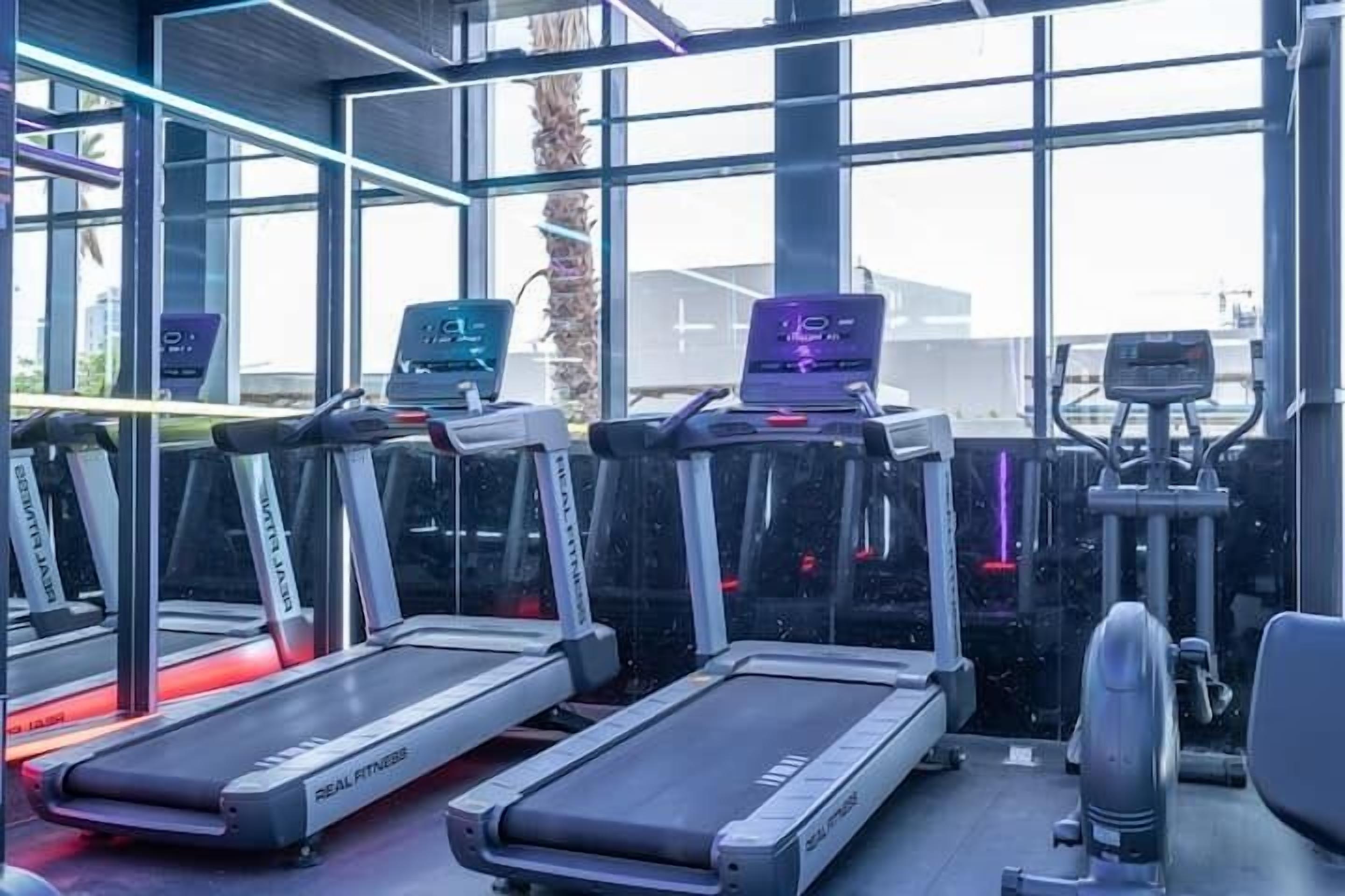 Une salle de sport équipée de plusieurs tapis de course, de vélos d’exercice et d’appareils de musculation.