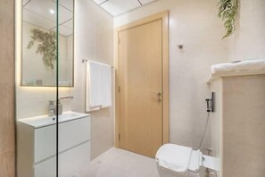 A modern bathroom with a glass shower enclosure, a wooden door, and a white sink. - Vogue JVC - Regina Tower (Dubai)