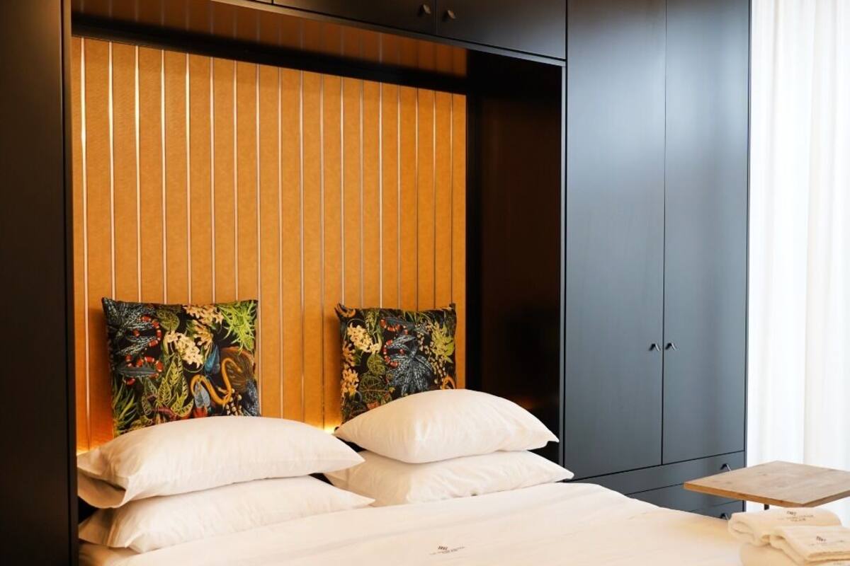 A hotel room with a bed, two pillows, a wooden headboard, a nightstand, and a hanging light fixture.