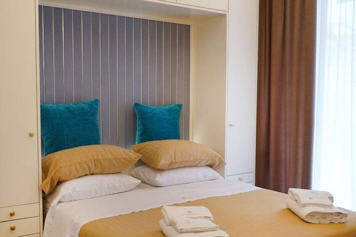 A neatly made bed with a yellow bedspread, two pillows, and a folded towel on the side.