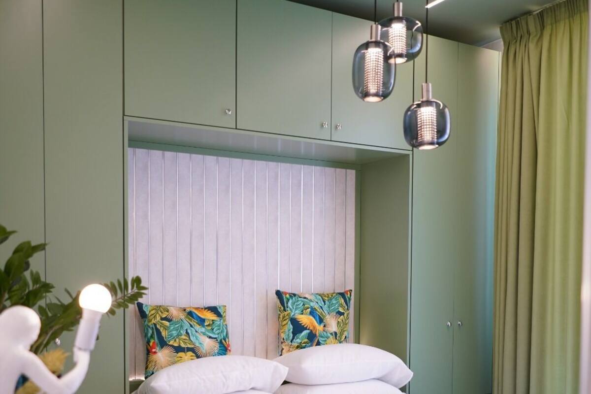 A modern bedroom with a green accent wall, a white bed with decorative pillows, and a ceiling light fixture.