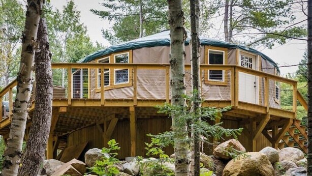 Una casa en un árbol con terraza de madera y varias ventanas, rodeada de rocas y árboles.