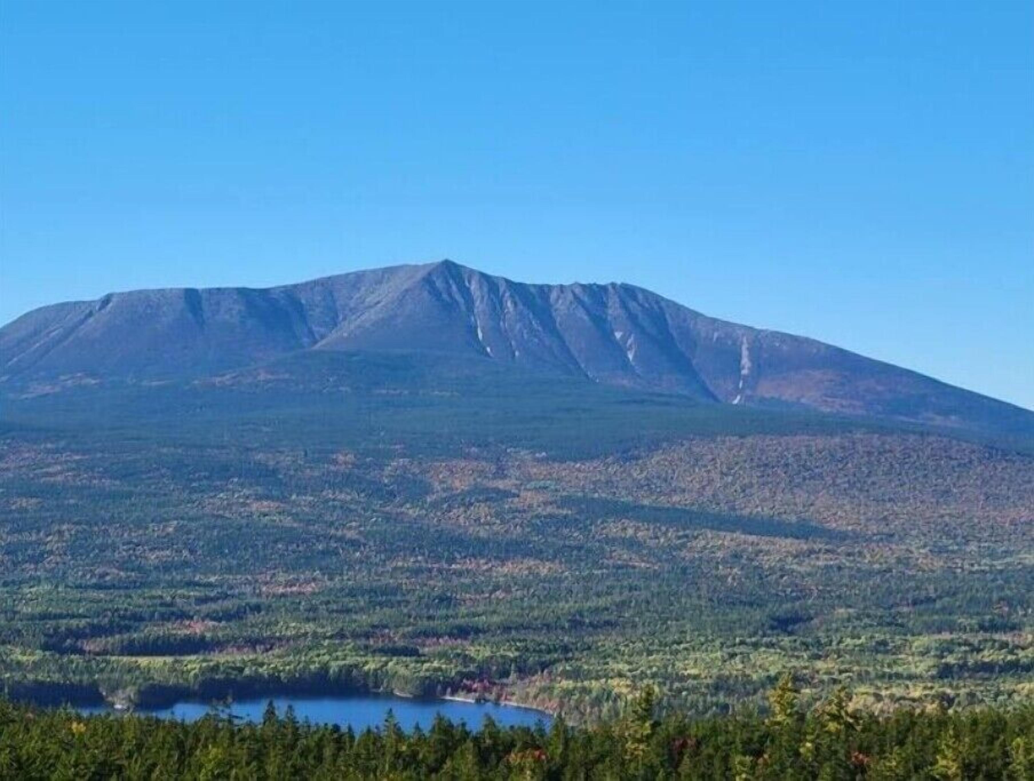 Ein Berg mit einem See am Fuße und einem bewaldeten Vordergrund.