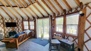 Una habitación acogedora con techo inclinado, vigas de madera, una cama, una mesa con una silla y ventanas amplias.