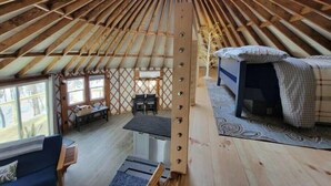 Una yurta espaciosa con un tragaluz central, una cama, una mesa y un sofá.