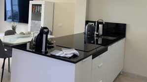 A modern kitchen with a black countertop, white cabinets, and a built-in coffee machine. - Sunset Harbour Costa Adeje Beautiful 2 bedrooms apartment with amaizing sea view (Tenerife)