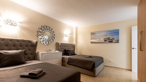 A bedroom with two beds, a nightstand, a wall-mounted mirror, and a painting of boats on water. - Sunset Harbour Costa Adeje Beautiful 2 bedrooms apartment with amaizing sea view (Tenerife)