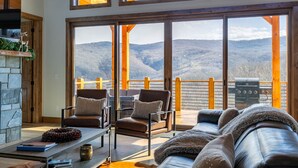 Un salon chaleureux avec une cheminée en pierre, des canapés en cuir et une grande fenêtre donnant sur un paysage montagneux.