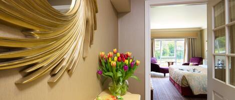 Ein Hotelzimmer mit einem Bett, einem Sessel, einem Schreibtisch mit Blumenvase und einem Spiegel an der Wand.