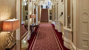 A grand hallway with a red carpet, ornate white walls, and a chandelier. - Manor House Country Hotel (Enniskillen)