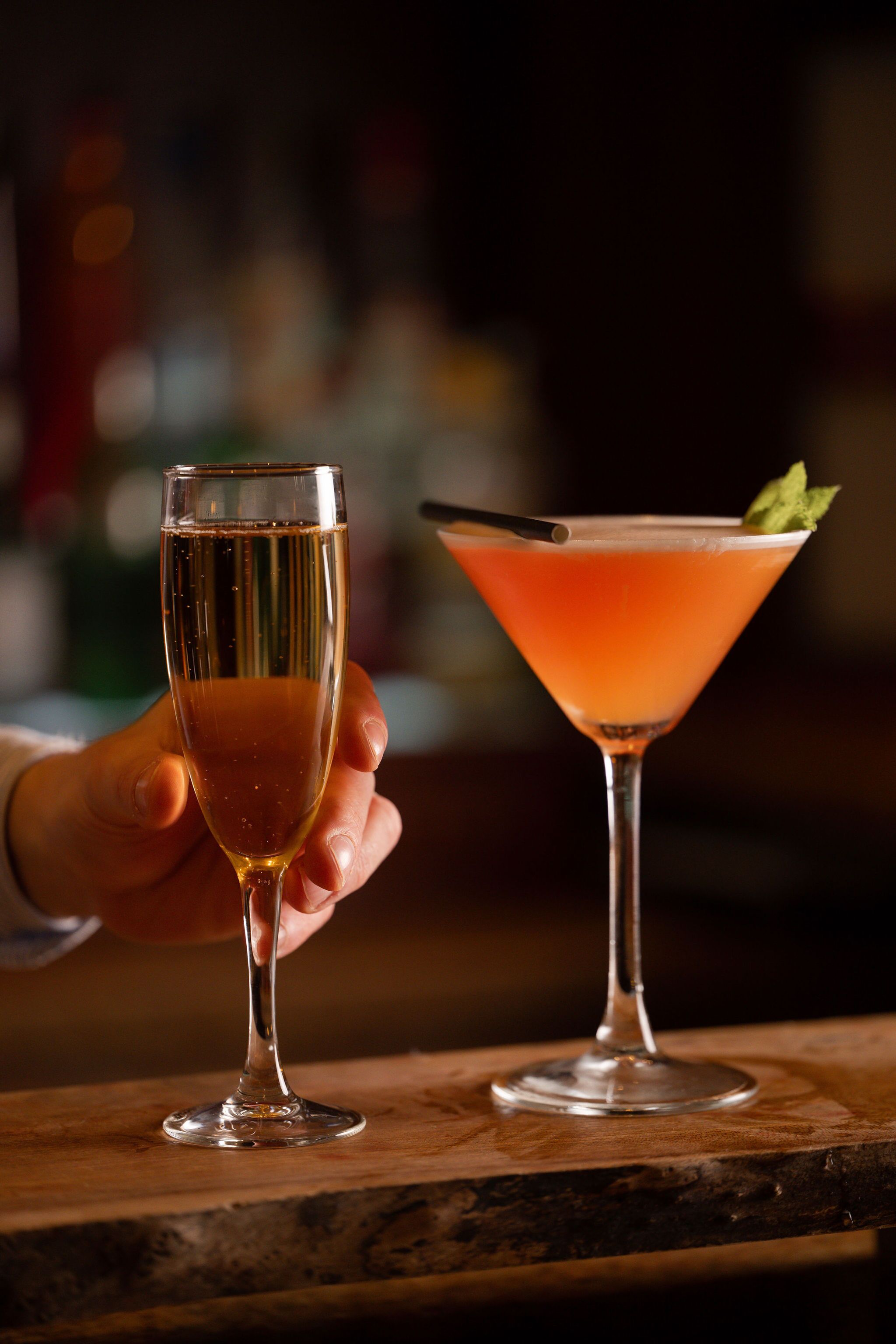 Two glasses of beverages on a wooden bar counter.