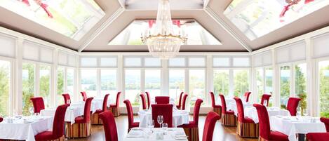 Une salle à manger avec des tables dressées, de grandes fenêtres et un lustre.