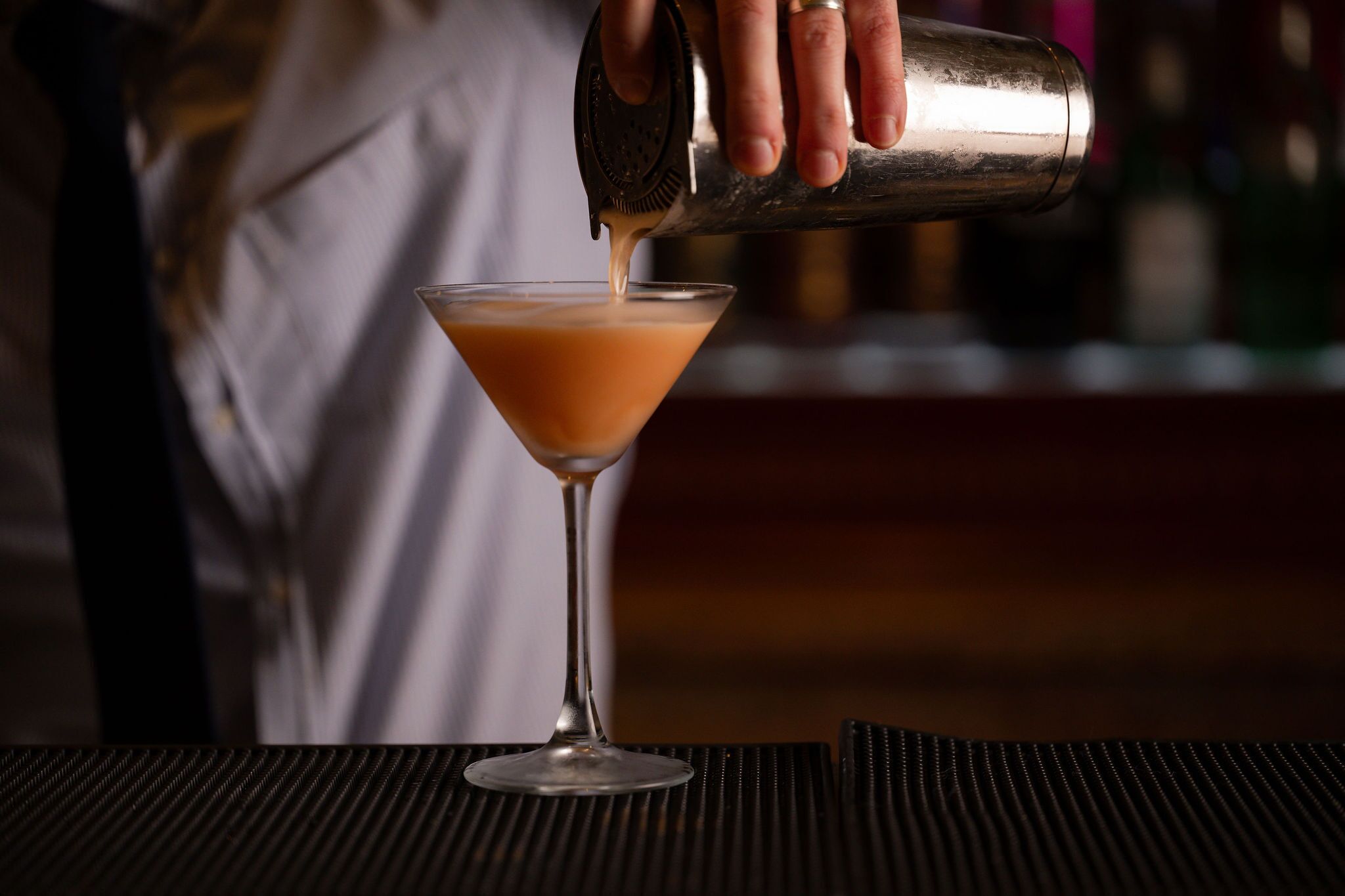 A person pouring a drink into a martini glass.