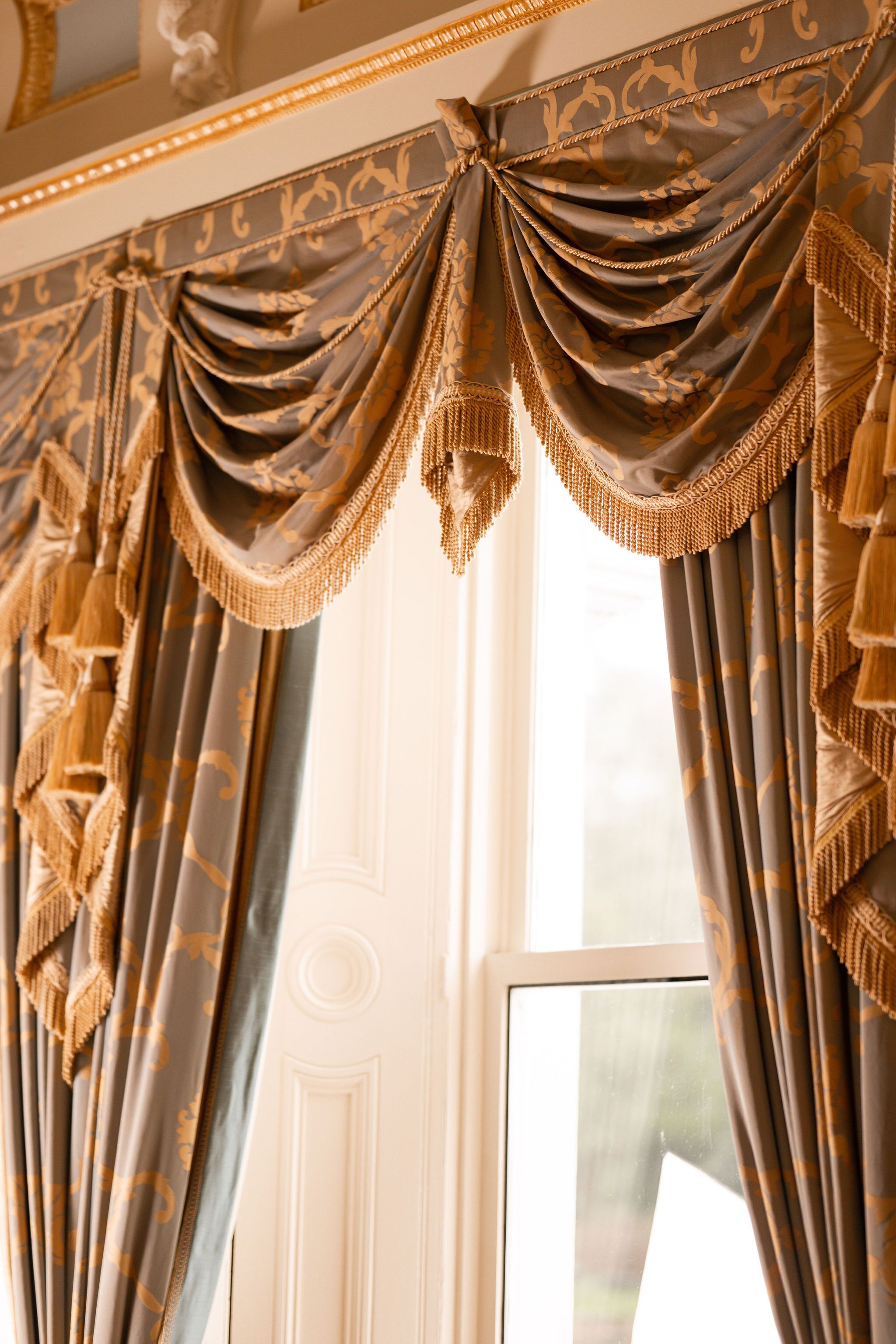 A window with ornate curtains featuring tassels and a decorative top.