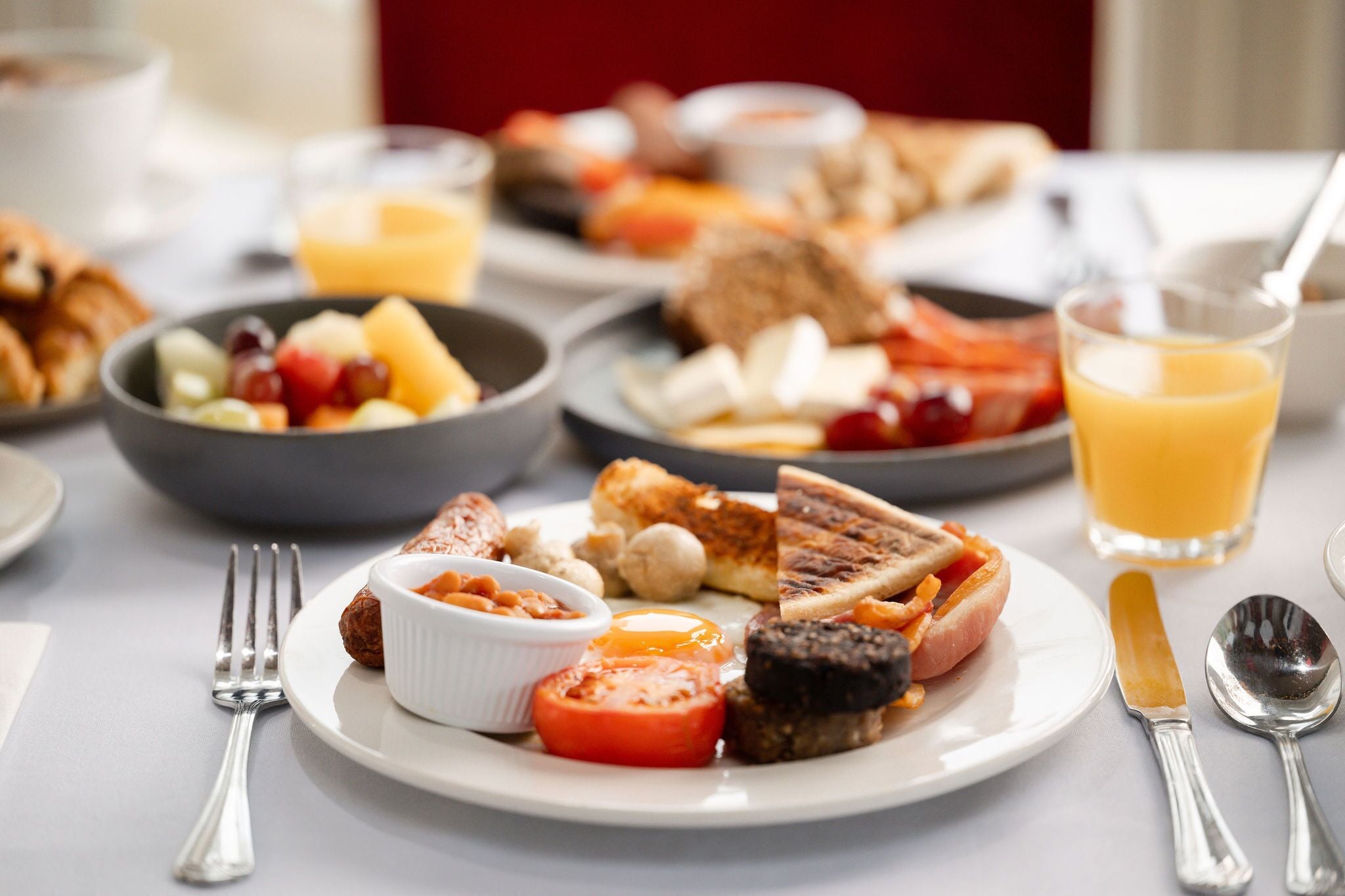 A breakfast setting with various dishes, including toast, eggs, tomatoes, and a glass of orange juice.