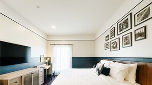 A hotel room with a large bed, a desk with a computer, a flat-screen TV, and a wall with framed pictures. - The Carpentry Hotel (Dalton)