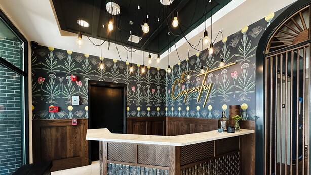 A reception area with a wooden counter, decorative wall with floral patterns, and hanging light fixtures. - The Carpentry Hotel (Dalton)