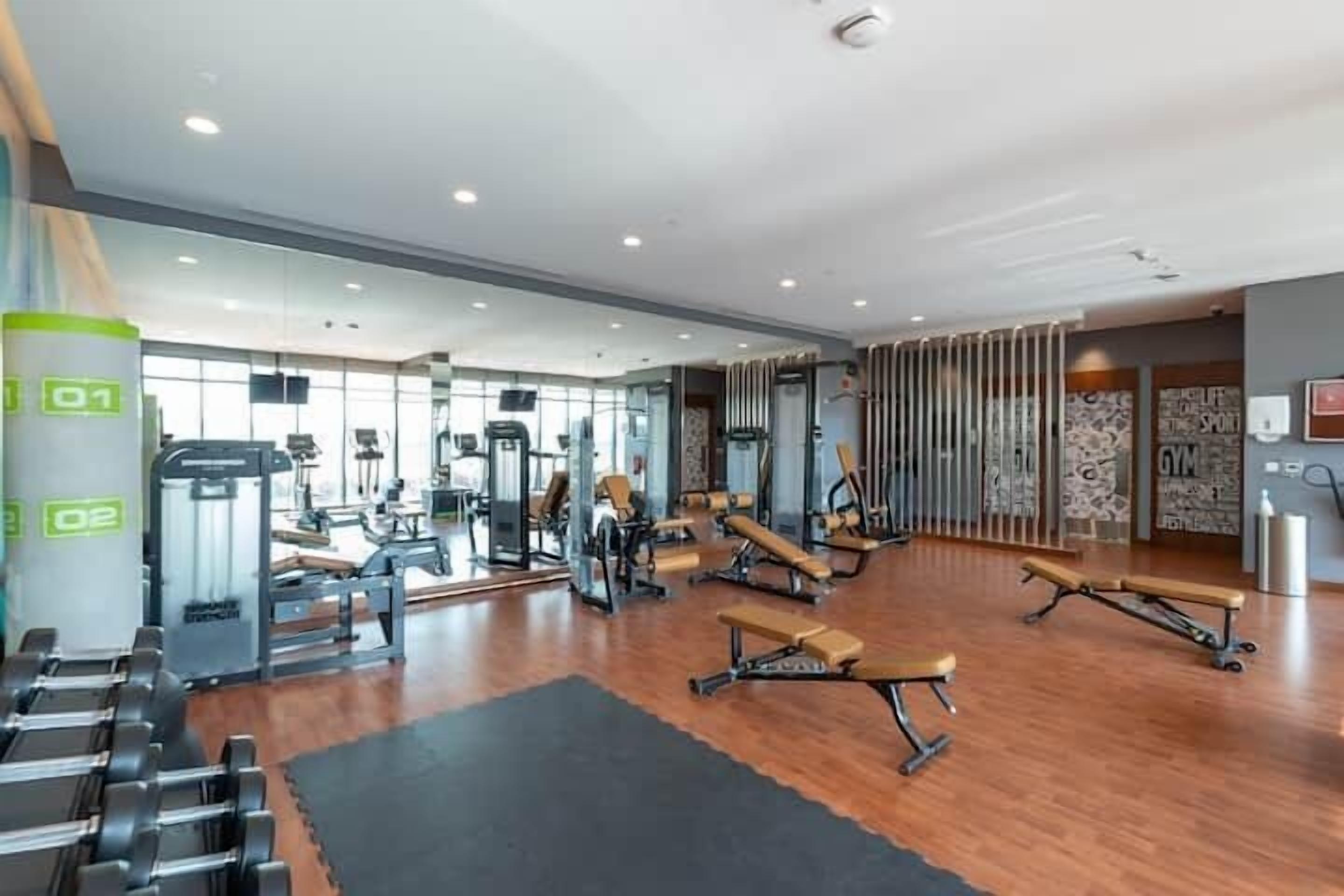 Ett modernt gym med olika typer av träningsutrustning, trägolv och en stor spegelvägg.
