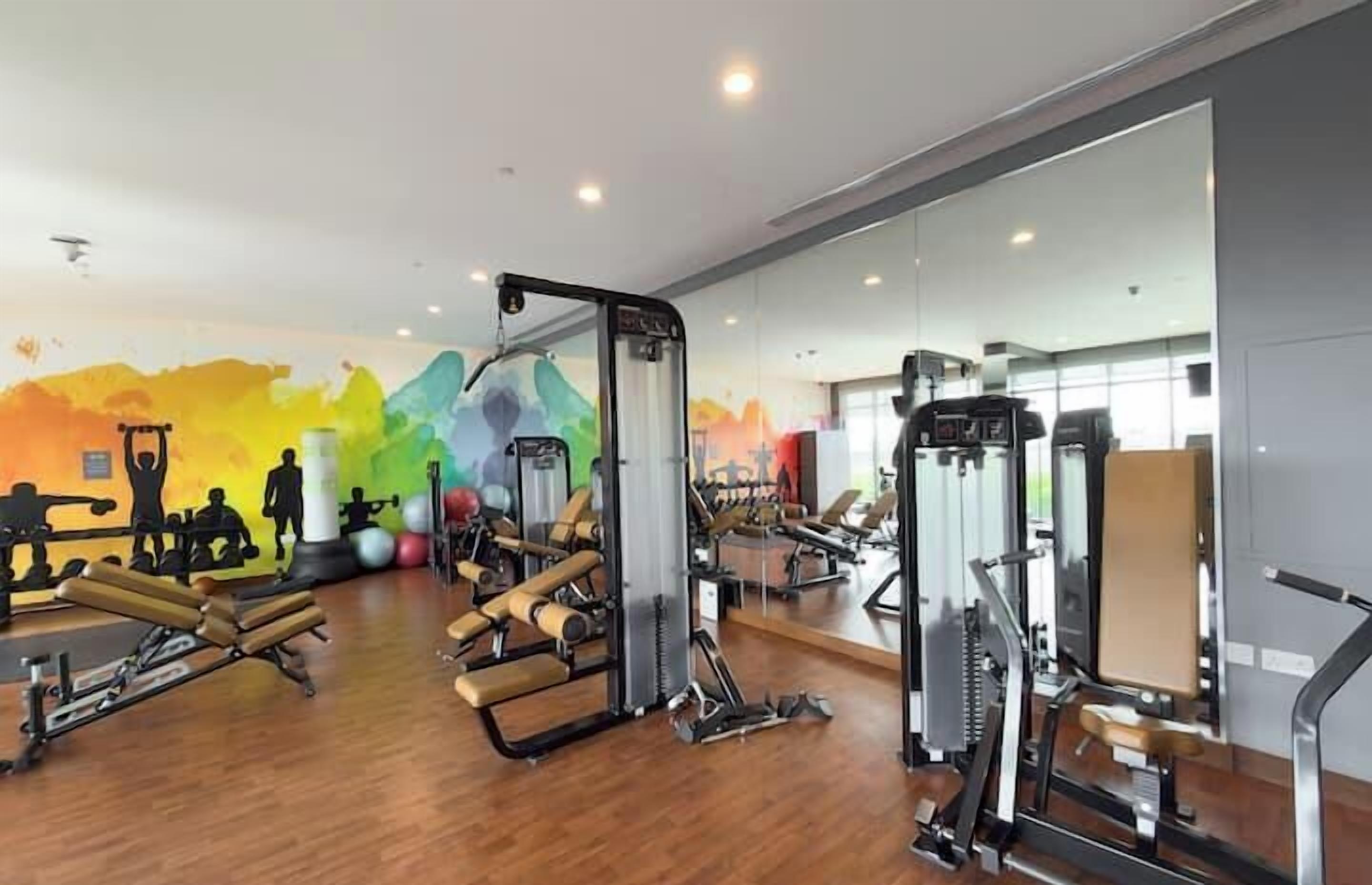 A gym with various exercise machines, a wooden floor, and a colorful mural on the wall.