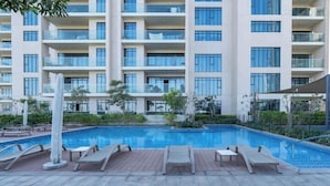 Um edifício moderno com piscina, cadeiras de descanso e um jardim bem cuidado.