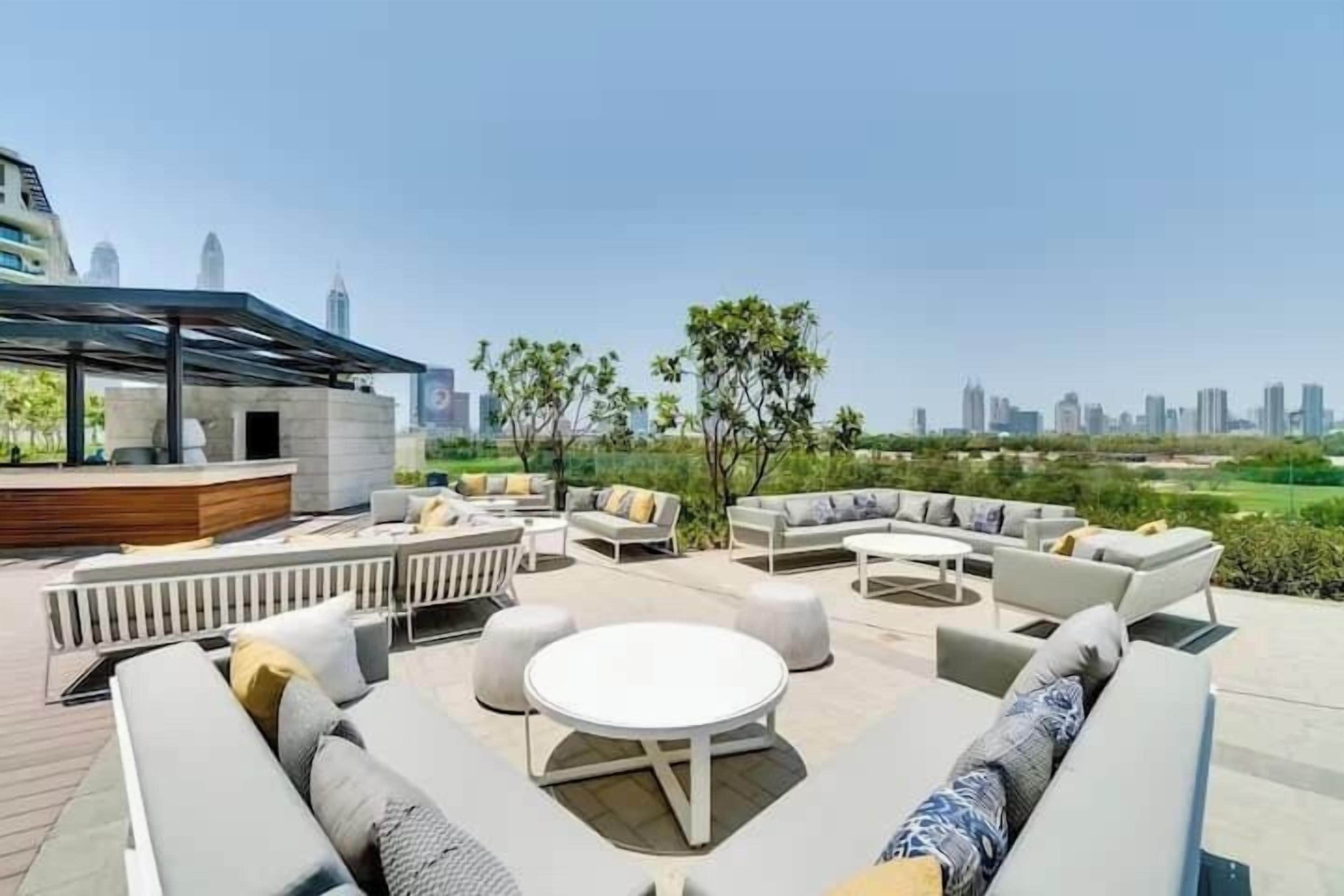 A rooftop lounge with outdoor seating, a bar area, and a city skyline view.