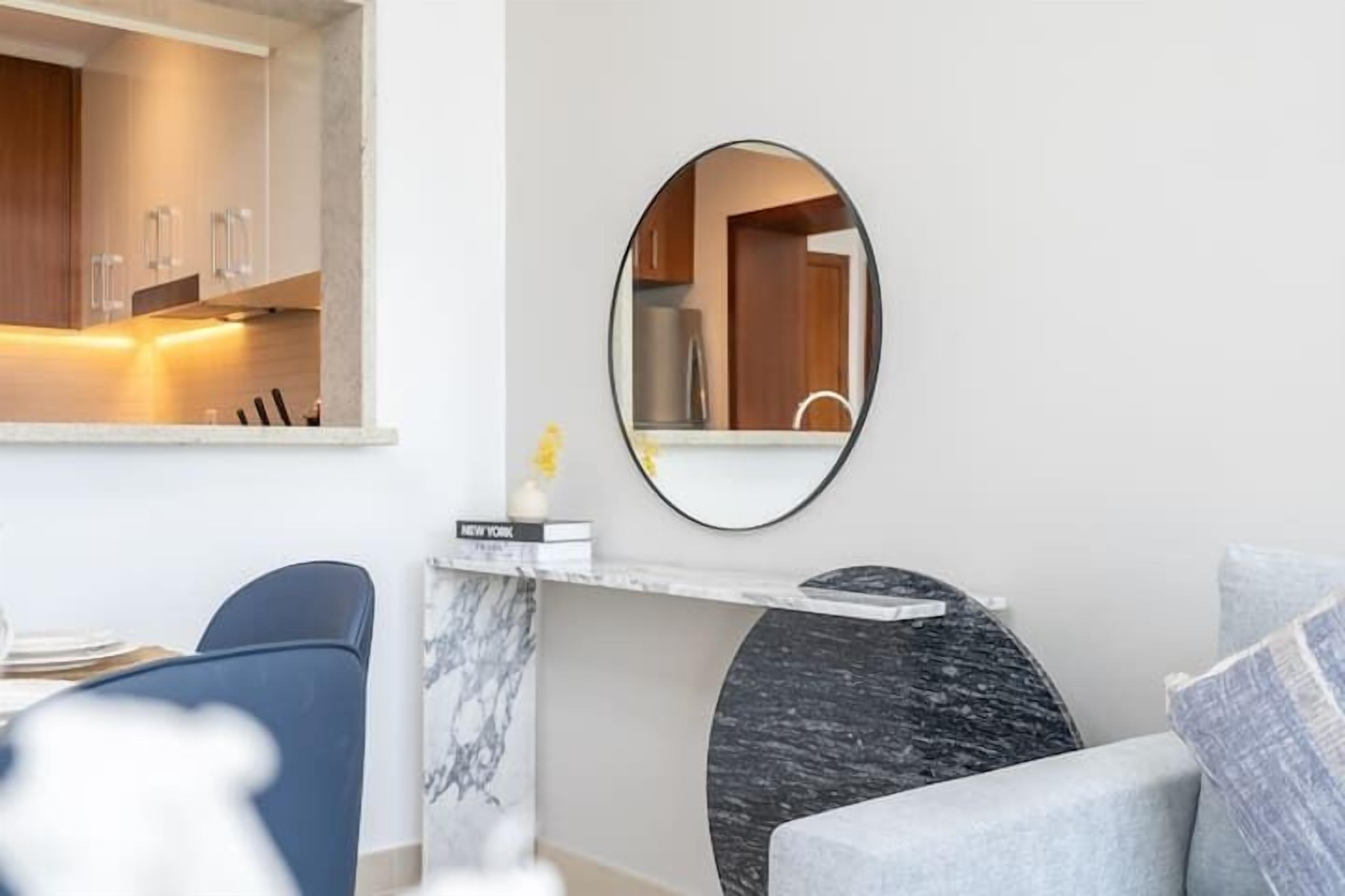 A modern living room with a marble fireplace, a round mirror, and a sofa.