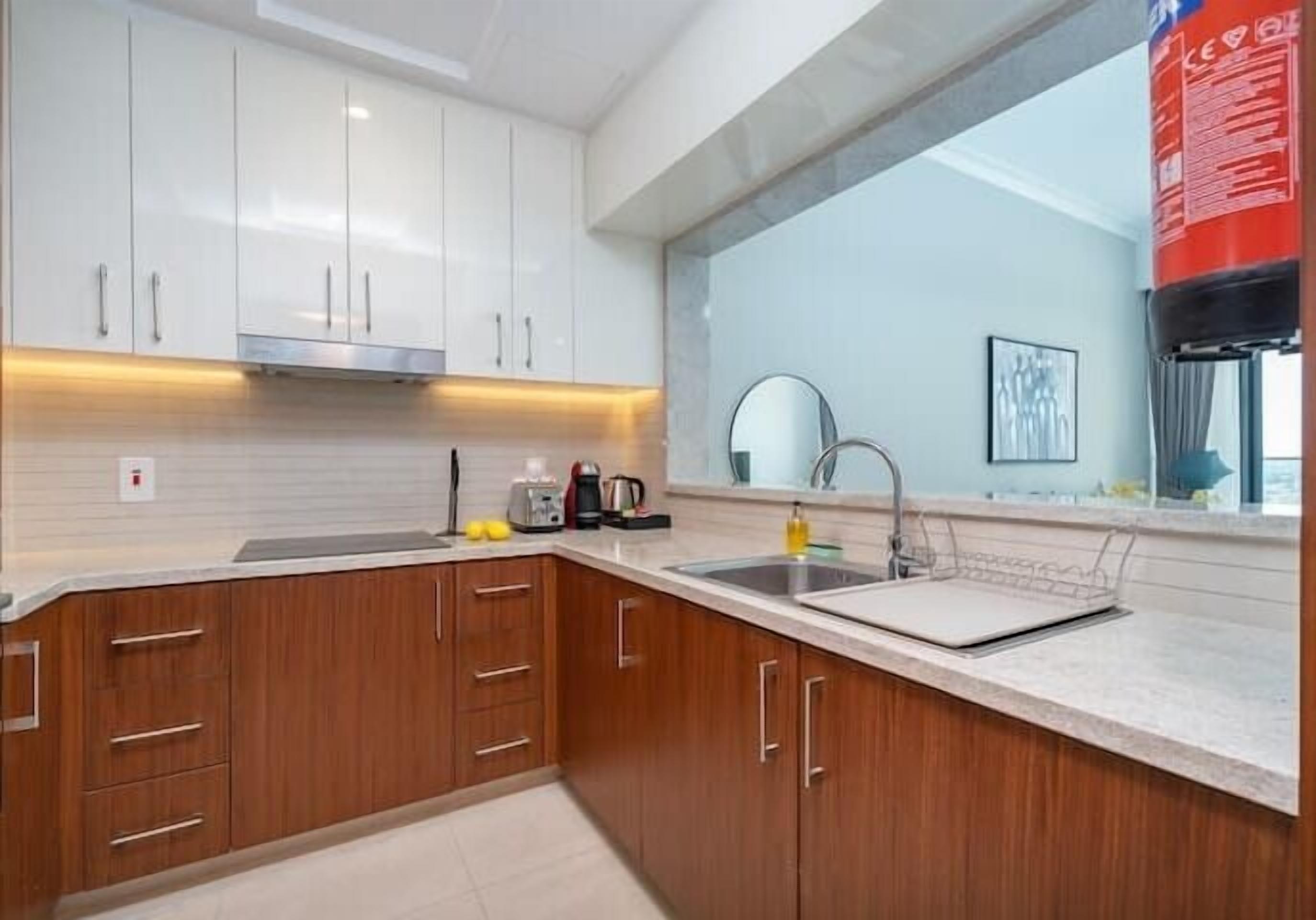 A modern kitchen with white cabinets, a stainless steel sink, and a countertop with a coffee maker and toaster.